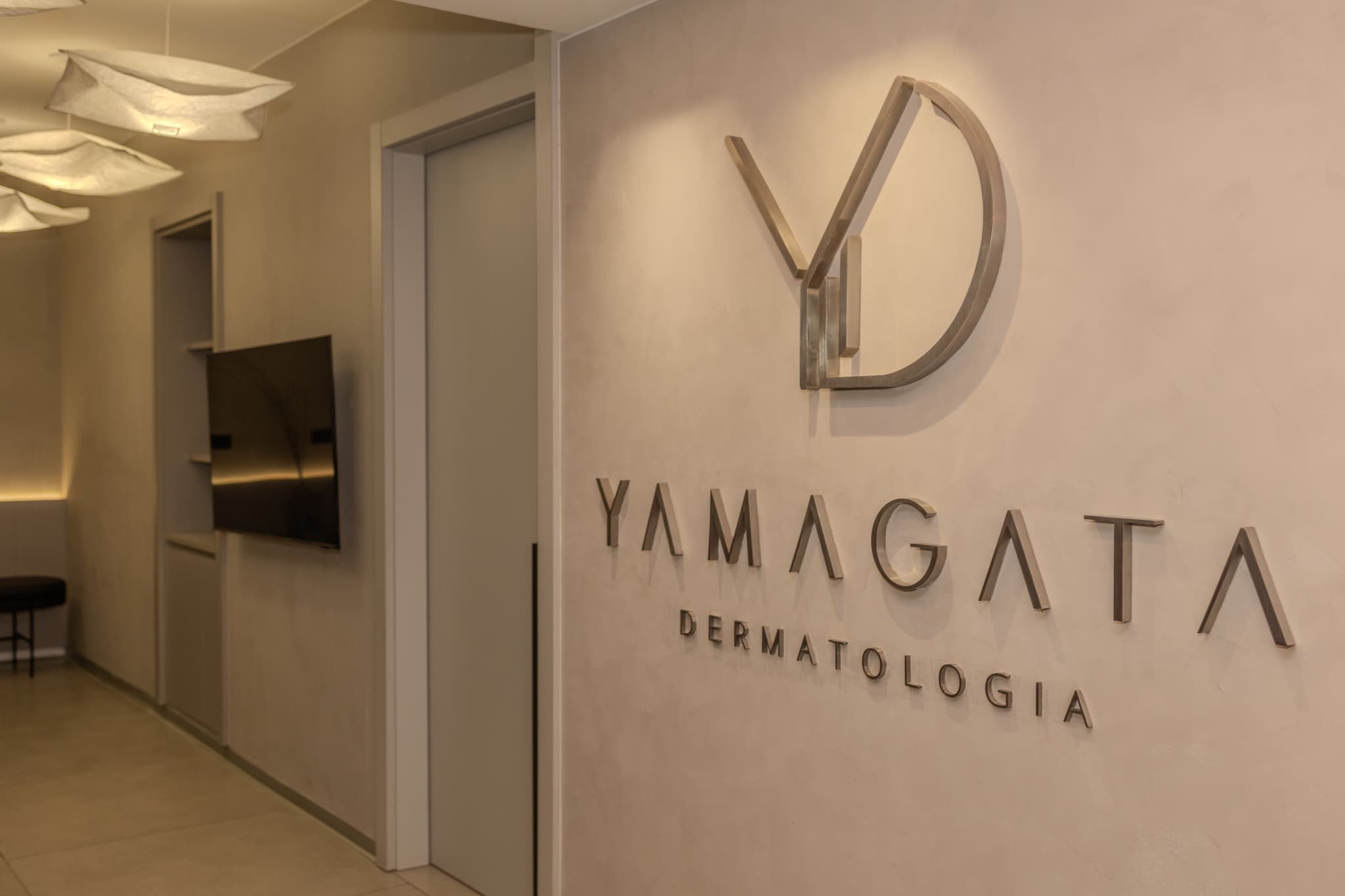 Recepção da Yamagata Dermatologia, com o logotipo da clínica na parede e poltronas em tons neutros